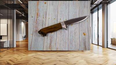 A hunting knife with a handle made of brown wood on a gray wooden table. Tools, edged weapons, hobbies, hunting. Wall mural