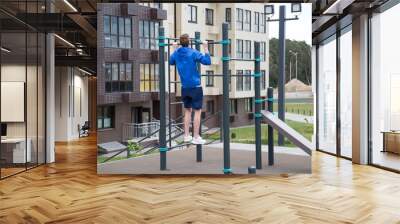 The athlete is pulled up on the crossbar of the simulator on the Playground in the city outdoors. Sport is a healthy lifestyle Hobby. Wall mural