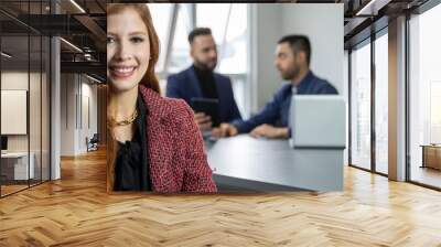 young woman looks at the camera smiling, in the background two men talk, blurred background Wall mural