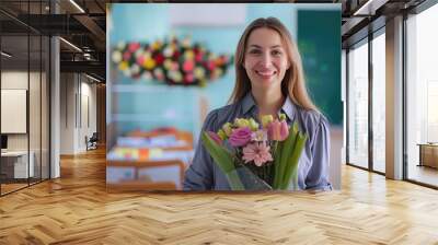 A smiling female teacher stands in a classroom setting, holding a bouquet of flowers while looking at the camera Wall mural