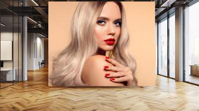 Beauty portrait of blonde woman with red lips, long healthy shiny blond hair style and manicured nails looking at camera. Sensual girl with bright makeup isolated on beige backhround. Wall mural