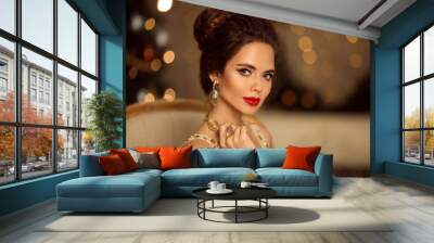 Beauty portrait of elegant woman with wedding hairstyle and makeup. Beautiful brunette girl with golden jewelry in prom dress sitting on modern chair over bokeh lights xmas decorations. Wall mural