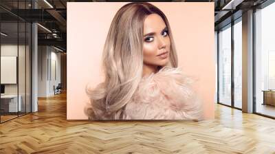 Ombre blond hairstyle. Beauty fashion blonde portrait. Sexy woman wears in pink fur coat. Beautiful girl model with makeup, long healthy hair style posing isolated on studio beige background. Wall mural