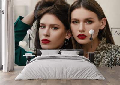 Close up portrait of two young beautiful fashionable women with red lips makeup, wearing trendy accessories and clothes, posing in street Wall mural