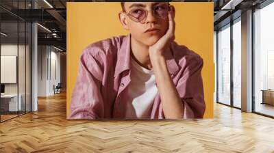 Close up studio fashion portrait of young man wearing trendy sunglasses, silk lilac color shirt, white t-shirt, posing on yellow background
 Wall mural