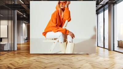 Fashionable confident blonde woman wearing trendy orange sweatshirt, white skinny jeans, high leather boots, posing on white background. Full-length stuido portrait Wall mural