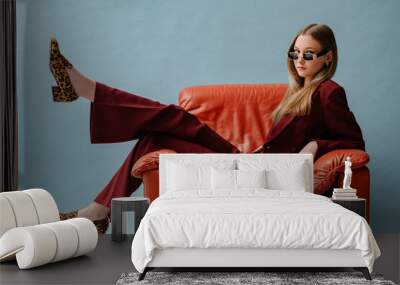 Fashionable confident woman wearing elegant marsala color suit, sunglasses, leopard print loafer shoes, posing, sitting in brown leather armchair. Studio fashion portrait. Copy. empty space for text Wall mural