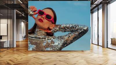 Fashionable confident woman wearing trendy fuchsia color rectangular sunglasses, sequin  turtleneck top, posing outdoor, against blue sky. Close up fashion portrait. Copy, empty space for text Wall mural