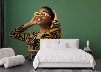 Fashionable happy smiling Black woman wearing trendy yellow rectangle sunglasses, animal, tiger print blouse, posing on green background. Copy, empty space for text Wall mural