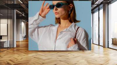 fashionable young woman wearing trendy blue sunglasses, oversized white linen shirt, posing on blue  Wall mural