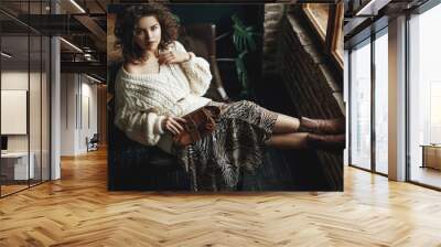 Full body fashion portrait of young beautiful confident woman wearing cozy white knitted sweater, animal print skirt, cowboy style boots, holding small brown bag, posing at loft interior Wall mural