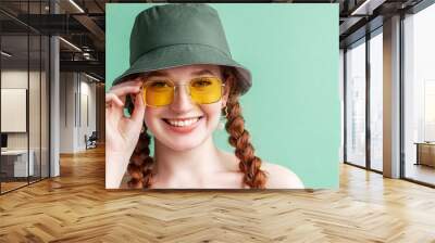 Happy smiling fashionable woman wearing yellow square sunglasses, trendy green bucket hat. Close up portrait. Copy, empty space for text Wall mural