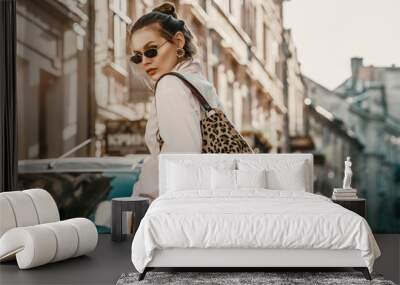 Outdoor autumn fashion portrait of elegant, luxury woman wearing sunglasses, trendy white shirt, leather trousers, with animal, leopard print bag, walking in street of European city. Copy, empty space Wall mural