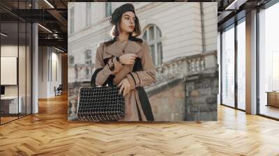 Outdoor autumn fashion portrait of young elegant lady wearing trendy faux leather beret, classic beige trench coat, holding black tweed bag, handbag. Copy, empty space for text Wall mural