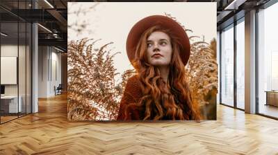 Outdoor close up portrait of young attractive redhead girl with natural freckled skin, long curly hair, wearing stylish orange hat, posing in beautiful autumn nature. Copy, empty space for text Wall mural