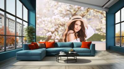 Outdoor close up portrait of young beautiful happy smiling woman with long dark hair, makeup, wearing straw hat, white blouse, posing near blooming tree. Copy, empty space for text Wall mural