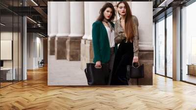 Outdoor fashion portrait of two young beautiful women wearing trendy clothes, accessories with animal print, holding black leather bags, posing in street of european city. Copy, empty space for text Wall mural