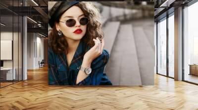 Outdoor fashion portrait of young beautiful fashionable girl wearing trendy sunglasses, wrist watch, earrings, leather beret, blue checkered dress, posing in street, on stairs. Copy, empty space Wall mural