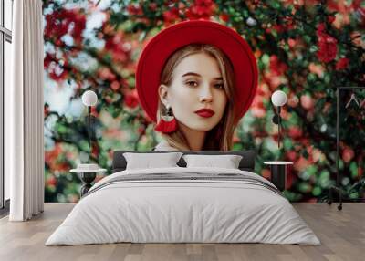 Outdoor portrait of young beautiful girl with red lips, long blonde hair, wearing hat, long tassel earrings, cold shoulder dress, posing near blooming tree. Summer fashion concept. Copy space  Wall mural