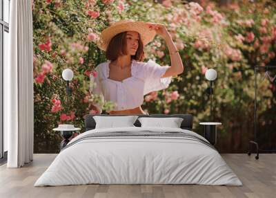 Summer street style, fashion portrait of woman wearing trendy summer outfit with straw hat, stylish  white blouse, denim shorts, posing in street, near blooming roses. Copy, empty space for text
 Wall mural