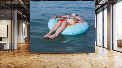 girl in leopard bikini relaxing lying down on top of the inflatable ring in crystal blue water Wall mural