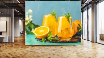 Two glass of orange ice drink with fresh mint on wooden turquoise table surface. Fresh cocktail drinks with ice fruit and herb decoration. Alcoholic non-alcoholic beverage Wall mural