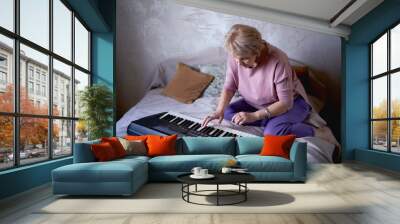  A 60-year-old mother and a 40-year-old daughter play the keyboard together on the bed at home Wall mural