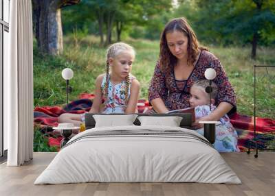 a mother and her two daughters read the holy bible and pray at an Easter picnic Wall mural