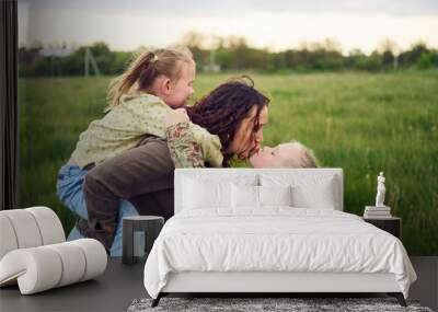 a mother rolls her daughters on her back, playing horse, kisses and hugs Wall mural