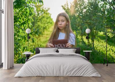 a teenage girl prays with a holy bible in a garden illuminated by light Wall mural