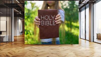 a teenage girl prays with a holy bible in a garden illuminated by light Wall mural