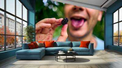 a young man eats a mulberry, has stained his hands, tongue, and face with the juice Wall mural