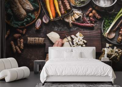 Female hands chopping celery on dark rustic kitchen table background with various vegetables and utensils. Root vegetables cooking preparation for tasty autumn dishes, top view. Healthy eating concept Wall mural