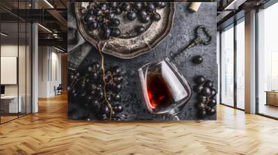 Red wine concept with glass, grapes in old plate and vintage corkscrew on dark table background, top view Wall mural