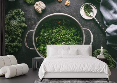 Stewed kale in cooking pot on dark kitchen table background with ingredients and spoon, top view Wall mural