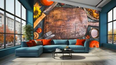 Thanksgiving dinner background with  turkey ,sauce,grilled vegetables,corn ,cutlery ,  pumpkin, fall leaves and flowers arrangements around wooden gutting board, top view. Wall mural