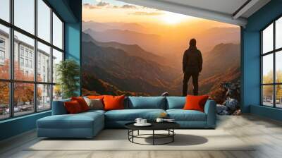 A lone adventurer stands on a mountain peak, overlooking a vast landscape as the sun rises. The scene exudes a sense of accomplishment, adventure, and the beauty of nature's vastness. Wall mural