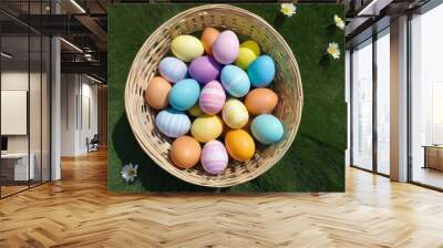 Vibrantly colored Easter eggs nestled in a wicker basket on a lush green lawn dotted with daisies, symbolizing springtime festivities. Wall mural