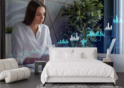 Attractive businesswoman in white shirt at workplace working with laptop to optimize trading strategy at corporate finance fund. Forex chart hologram over office background Wall mural