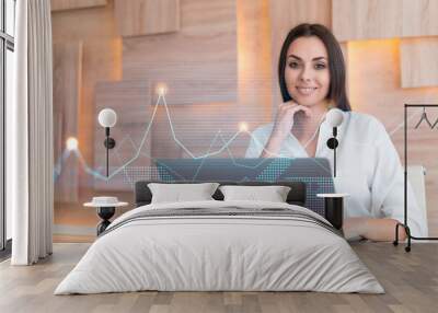 Attractive businesswoman in white shirt at workplace working with laptop to optimize trading strategy at corporate finance fund. Forex chart hologram over office background Wall mural