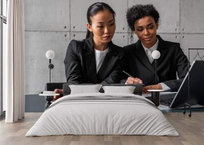 Smiling young African woman and her Asian colleague working together at loft office table with laptop. Concept of education and management Wall mural