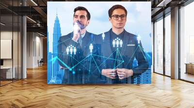 Two handsome young SMM specialists thinking about development of social media marketing strategy to achieve business goals. Hologram icons over Kuala Lumpur background. Wall mural