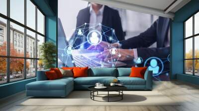 Two HR specialists in formal wear analyzing the recruitment market using laptop to boost the intern program at international consulting company. Social networking hologram icons. Wall mural