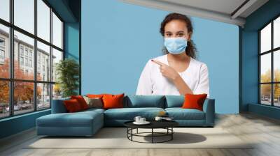 African american doctor woman isolated on blue background. Female doctor in white medical gown sterile face mask pointing index finger aside. Healthcare personnel medicine concept. Mock up copy space. Wall mural