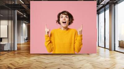 Amazed young brunette woman girl in yellow sweater posing isolated on pastel pink background, studio portrait. People sincere emotions lifestyle concept. Mock up copy space. Pointing index fingers up. Wall mural