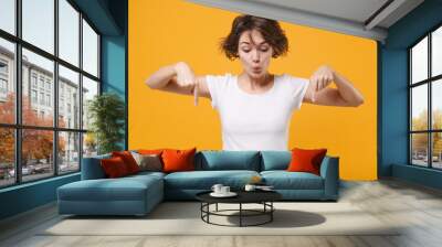 Amazed young brunette woman in white t-shirt posing isolated on yellow orange wall background studio portrait. People sincere emotions lifestyle concept. Mock up copy space. Point index fingers down. Wall mural