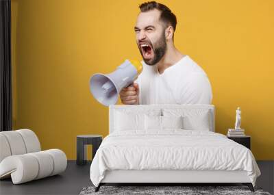 Angry young bearded man guy in white casual t-shirt posing isolated on yellow background studio portrait. People lifestyle concept. Mock up copy space. Scream in megaphone pointing index finger aside. Wall mural