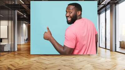 Back rear view of funny young african american man guy in casual pink t-shirt posing isolated on blue background studio. People lifestyle concept. Mock up copy space. Showing thumb up, looking camera. Wall mural