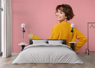 Back rear view of young brunette woman girl in yellow sweater posing isolated on pink wall background studio portrait. People lifestyle concept. Mock up copy space. Showing thumbs up, looking back. Wall mural