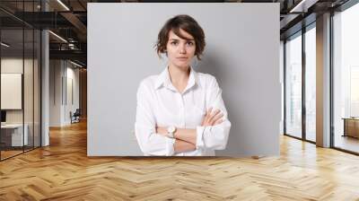 Beautiful young business woman in white shirt posing isolated on grey background studio portrait. Achievement career wealth business concept. Mock up copy space. Holding hands crossed, looking camera. Wall mural